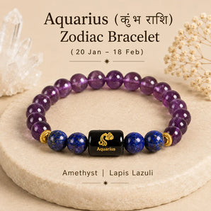 An Aquarius zodiac bracelet made of purple amethyst and blue lapis lazuli stones with a central black cube featuring gold Aquarius zodiac symbol, displayed on a beige stone slab with decorative crystals and dried flowers.