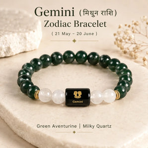 A Gemini zodiac bracelet made of Green aventurine and milky quartz beads with a central black cube bead featuring a gold Gemini zodiac symbol. The bracelet is displayed on a beige stone slab with decorative crystals and dried flowers in the background, with text overlays describing the product.