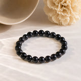 Black Obsidian bracelet with glossy jet-black crystal beads on cream draped fabric beside a ceramic bowl – World of Oorja