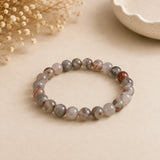 Bloodstone bracelet with mottled grey-green beads flecked rust red on beige paper with a white ceramic bowl – World of Oorja