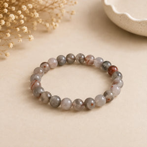 Bloodstone bracelet with mottled grey-green beads flecked rust red on beige paper with a white ceramic bowl – World of Oorja