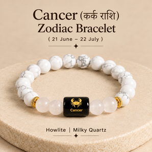 A Cancer zodiac bracelet made of white and gray marbled howlite and milky quartz beads, with a central black cube bead featuring a gold Cancer zodiac symbol and text. The bracelet is displayed on a beige textured pedestal with astrological text above and below.