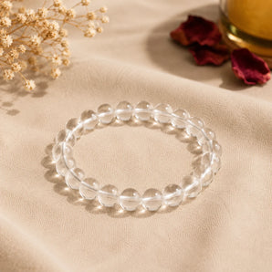 Clear Quartz Sphatik bracelet with transparent glassy beads on beige linen with rose petals and a brass vessel – World of Oorja