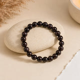 Garnet bracelet with deep wine-red glossy beads on a smooth cream stone with dried pampas and a lit candle – World of Oorja