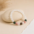 Pregnancy bracelet with milky moonstone beads and green, pink and peach accents draped over a beige pebble – World of Oorja
