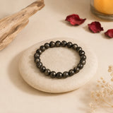 Pyrite bracelet with metallic golden-grey crystal beads on a cream pebble with driftwood, rose petals and a candle – World of Oorja