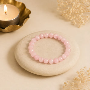 Rose Quartz bracelet with milky pink crystal beads on a pale pebble beside a lit brass tealight – World of Oorja