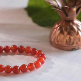 Red beaded bracelet on a white surface with a bronze pineapple-shaped object in the background.