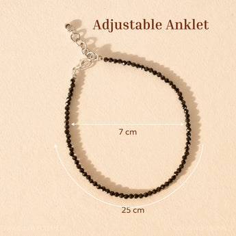 Black beaded anklet with adjustable strap on a beige background