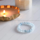 Light blue beaded bracelet on a white surface with a candle in the background.