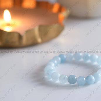 Blue beaded bracelet on a white surface with a blurred candle in the background