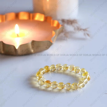 Yellow beaded bracelet on a white surface with a candle in the background
