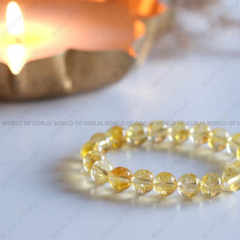 Yellow beaded bracelet on a white surface with a lit candle in the background