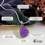 Purple amethyst pendant on a silver chain with labeled benefits, set against a dark fabric and dried flowers background.