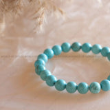 Turquoise beaded bracelet on a textured beige background with 'World of Oorja' branding.