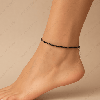 Black beaded anklet on a foot against a beige background