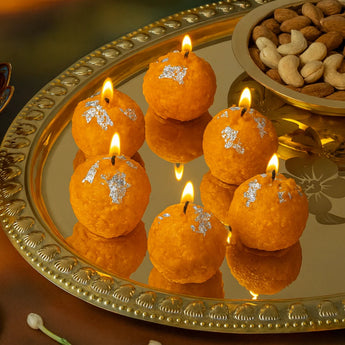 Decorative candles shaped like oranges with silver accents on a reflective surface, surrounded by nuts and flowers.