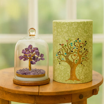 Decorative items including a amethyst tree under a glass dome and a cylindrical container with a tree design on a wooden table.