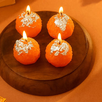 Four orange candles with decorative elements on a wooden surface.