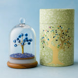 Decorative container with evil eye tree design and another with glass dome and blue tree inside on a light blue background.