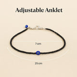 Adjustable anklet with black beads and blue evil eye charm on a beige background