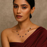 Woman wearing a maroon saree with a gold necklace against a beige background