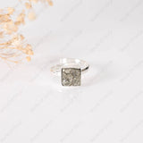 Silver ring with a square, textured design on a light background