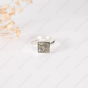 Silver ring with a square, textured design on a light background