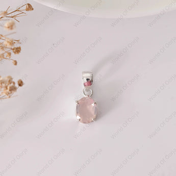 Pink gemstone pendant on a white background with dried flowers.