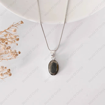Necklace with a pendant on a white surface with dried flowers.