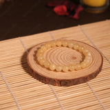 Round wooden coaster with a bracelet on a woven mat, candle in the background