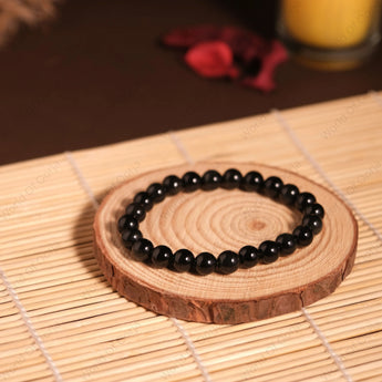 Black beaded bracelet on a wooden coaster with a candle in the background
