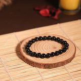 Black beaded bracelet on a wooden coaster with a candle in the background