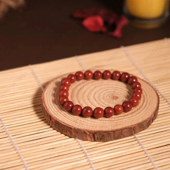 Red beaded bracelet on a wooden coaster with a candle in the background