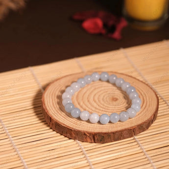 Two beaded bracelets on a wooden coaster with a candle in the background