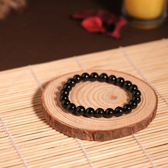 Black beaded bracelet on a wooden coaster with a candle in the background