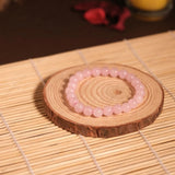 Pink beaded bracelet on a wooden coaster with a candle in the background