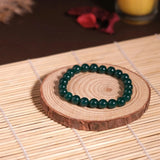 Green beaded bracelet on a wooden coaster with a candle in the background
