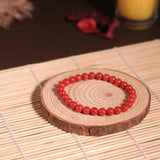 Red beaded bracelet on a wooden coaster with a candle in the background
