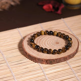 Bracelet with tiger eye beads on a wooden coaster with a candle in the background