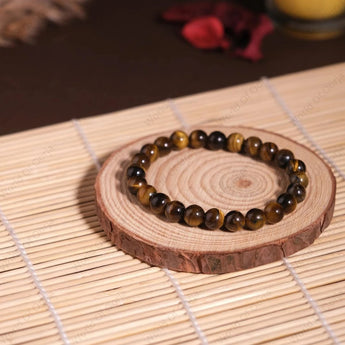 Bracelet with tiger eye beads on a wooden coaster with a candle in the background
