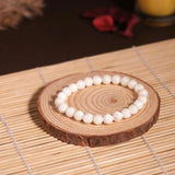 Pearl bracelet on a wooden coaster with a candle in the background