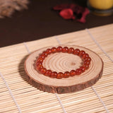 Red beaded bracelet on a wooden coaster with a candle in the background