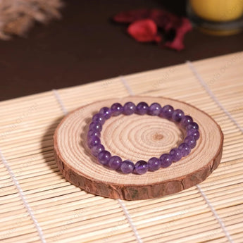 Purple beaded bracelet on a wooden coaster with a candle in the background