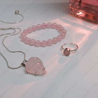 Pink crystal necklace, bracelet, and ring on a white surface with soft lighting.