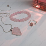 Pink crystal necklace, bracelet, and ring on a white surface with soft lighting.