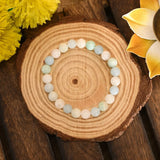 Round wooden coaster with a bracelet featuring multicolored beads, surrounded by yellow flowers on a wooden surface.