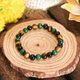 Beaded bracelet with green, black, and brown stones on a wooden surface