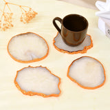 Set of four round stone coasters with orange rims on a light surface, one coaster holding a brown mug.