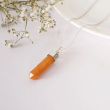 Necklace with an orange pendant on a white background with small white flowers.